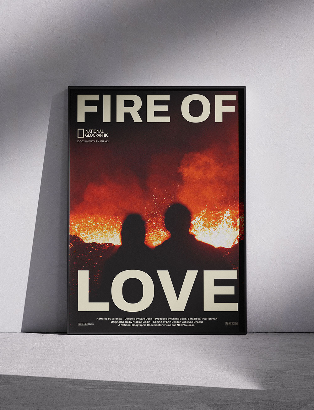 Affiche poster du film FIRE OF LOVE posé sur le sol, avec une photo de volcan en éruption et du couple en premier plan